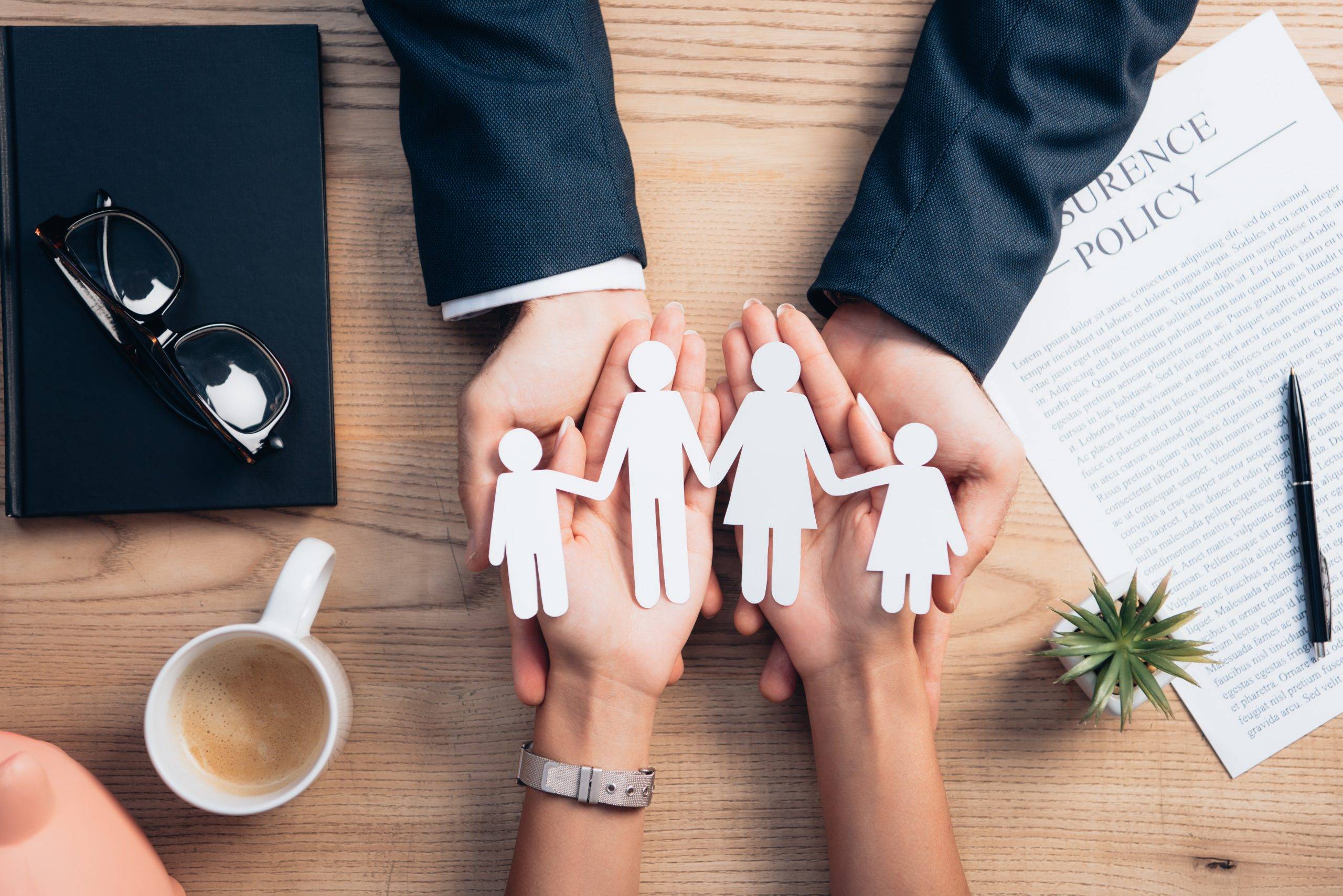 Top View Of Lawyer And Woman Holding Paper Cut Family Near Cup Of Coffee, Insurance Policy Agreement, Notebook And Plant Top View Of Lawyer And Woman Holding Paper Cut Family Near Cup Of Coffee, Insurance Policy Agreement, Notebook And Plant